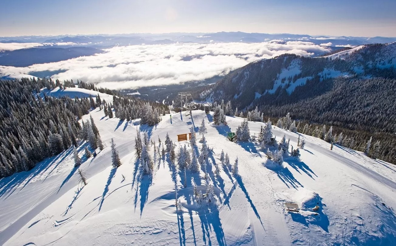 Aerial view of a snowy ski resort with a chairlift rising above a sea of clouds