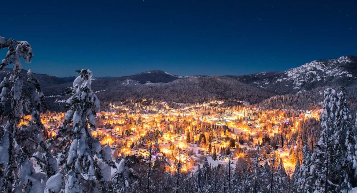 Aerial view of a river valley town at dusk with lights reflecting on the water